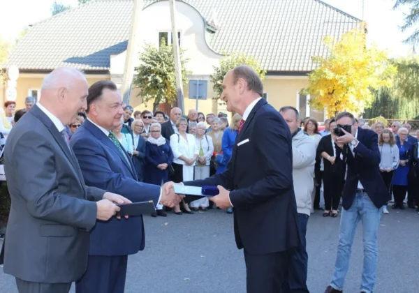 Uczestnicy uroczystości w garniturach wręczają sobie dokumenty podczas rewitalizacji najstarszej części Gąbina, otoczeni zgromadzonymi mieszkańcami i fotografem.