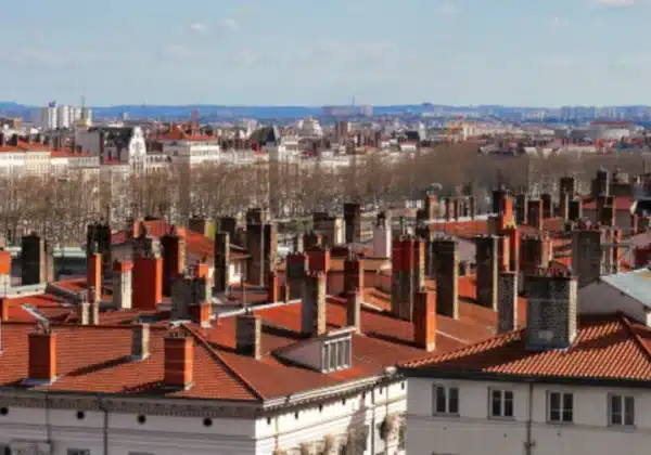 Panorama miasta z widokiem na dachy domów z czerwonymi dachówkami oraz kominami.