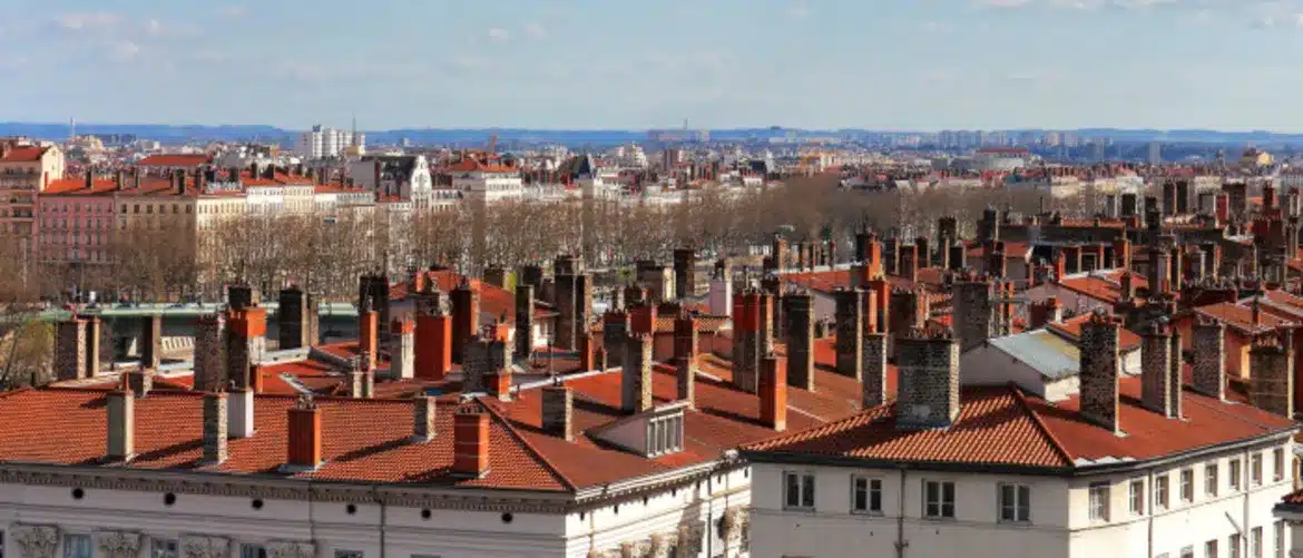 Panorama miasta z widokiem na dachy domów z czerwonymi dachówkami oraz kominami.