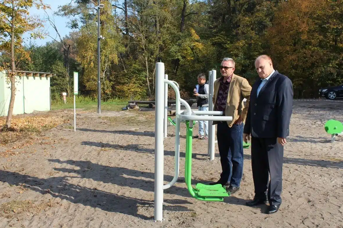 Na zdjęciu widać mężczyzn oglądających sprzęt do ćwiczeń w nowo powstającym miejscu wypoczynku nad Jeziorem Łąckim Dużym.