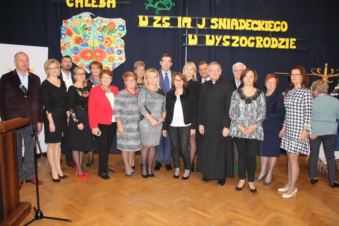 W wydarzeniu „Dzień Chleba” w Zespole Szkół im. J. Śniadeckiego w Wyszogrodzie uczestniczyli przedstawiciele społeczności lokalnej i pedagogicznej, pozując do wspólnego zdjęcia.