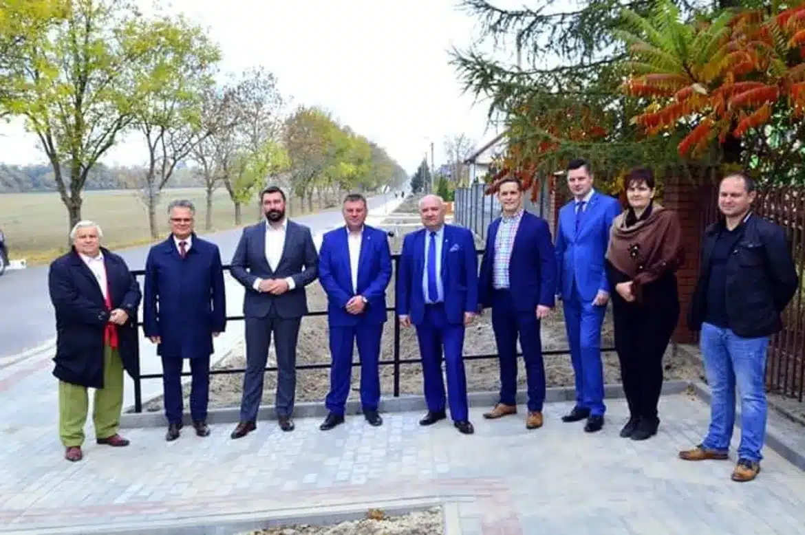 Na zdjęciu widać grupę osób w strojach formalnych, stojących obok nowego chodnika w Nowym Miszewie, z widokiem na otaczającą je zieleń.