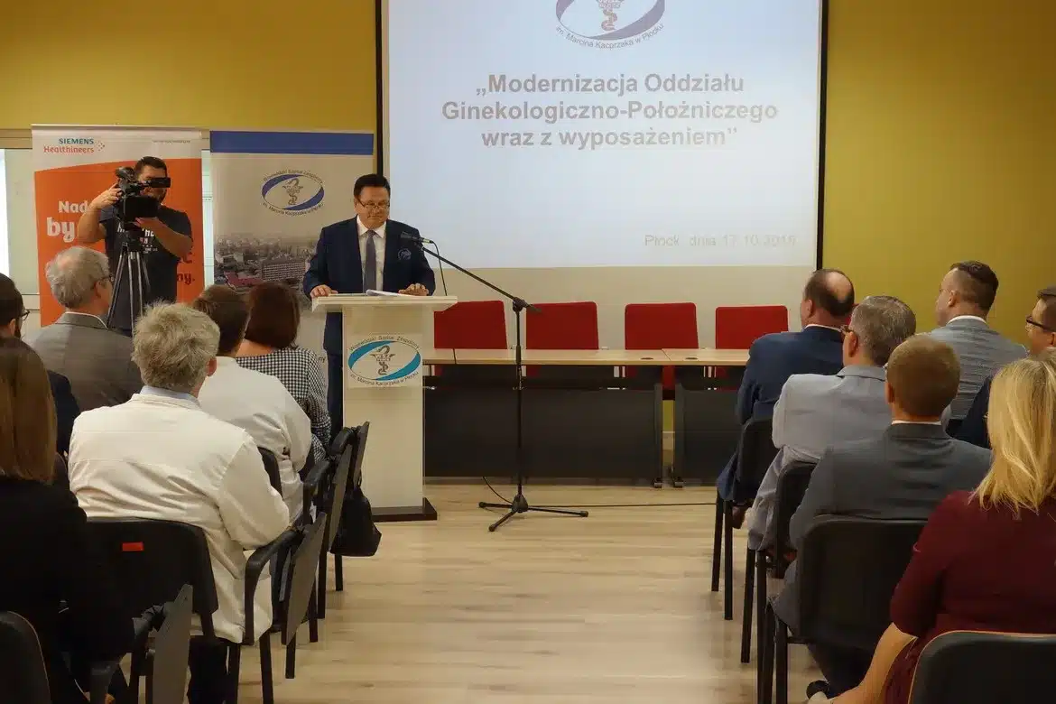 Na zdjęciu przedstawiono oficjalne otwarcie zmodernizowanego Oddziału Ginekologiczno-Położniczego w płockim Szpitalu Wojewódzkim, z mówiącym przedstawicielem i obecnymi gośćmi.