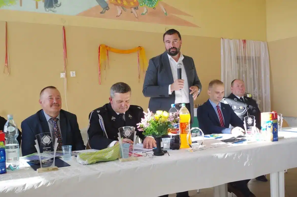 Na zdjęciu przedstawiono uczestników spotkania w OSP Juryszewo, w tym mężczyzn wygłaszających przemówienia oraz dekoracje przy stole, w atmosferze gratulacji dla druhów.