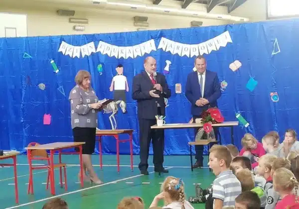 Uroczystość z okazji Dnia Edukacji Narodowej w Gminie Łąck, w której uczestniczą nauczyciele oraz dzieci zgromadzone na sali.