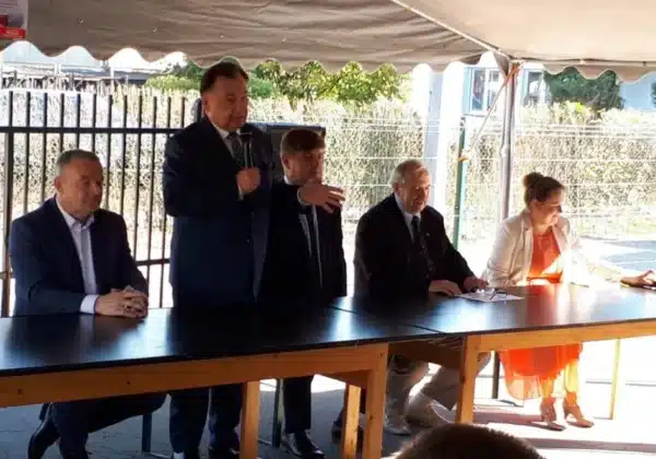 Na zdjęciu widać grupę osób siedzących przy stole podczas wydarzenia, w którym jeden z mężczyzn występuje z przemówieniem, najprawdopodobniej związanym z modernizacją drogi w Gminie Brudzeń Duży.