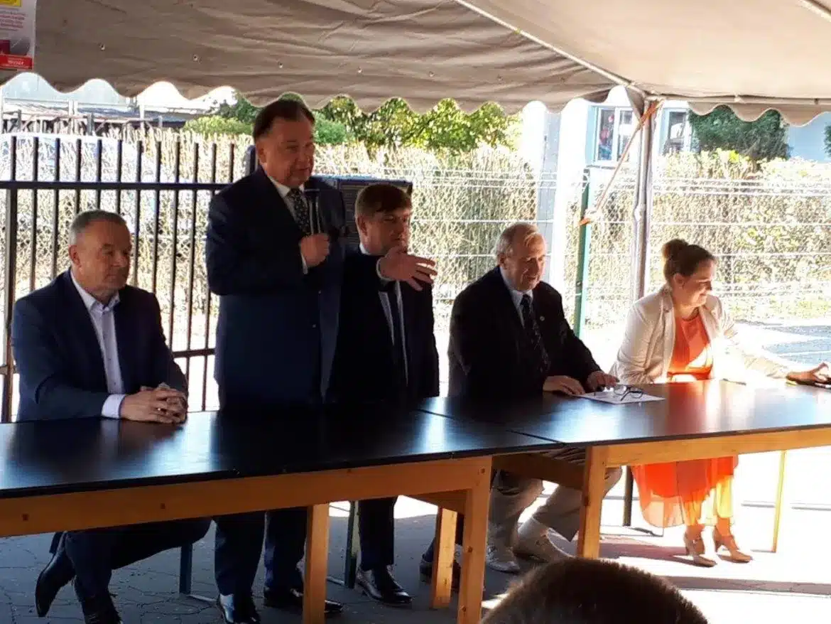 Na zdjęciu widać grupę osób siedzących przy stole podczas wydarzenia, w którym jeden z mężczyzn występuje z przemówieniem, najprawdopodobniej związanym z modernizacją drogi w Gminie Brudzeń Duży.