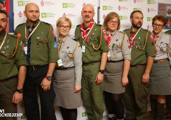 Grupa harcerzy w mundurach ZHP stoi do zdjęcia podczas Zjazdu Chorągwi Mazowieckiej ZHP, z identyfikatorami i naszywkami, w tle banery z logo ZHP.