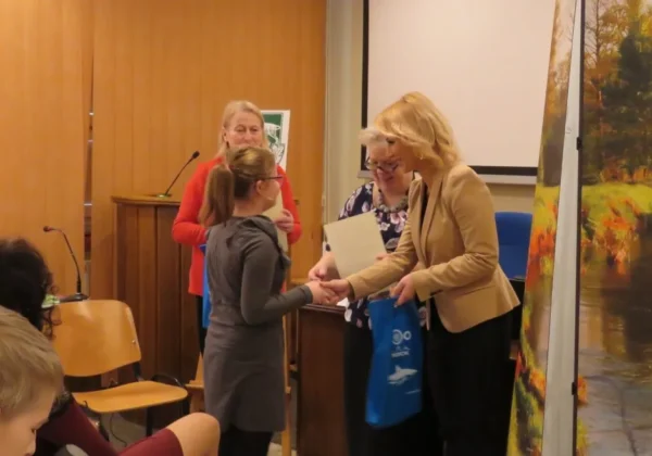 Podsumowanie konkursu ornitologicznego „Mój ulubiony ptak” – wręczanie nagrody młodej uczestniczce przez prowadzącą w sali.