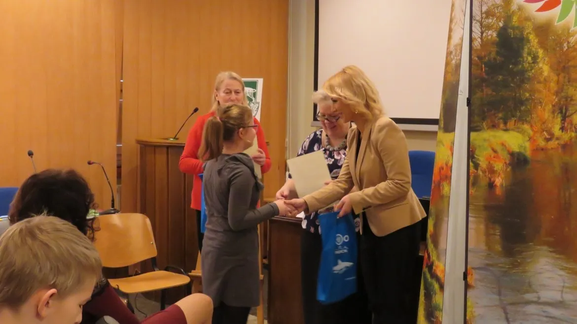 Podsumowanie konkursu ornitologicznego „Mój ulubiony ptak” – wręczanie nagrody młodej uczestniczce przez prowadzącą w sali.