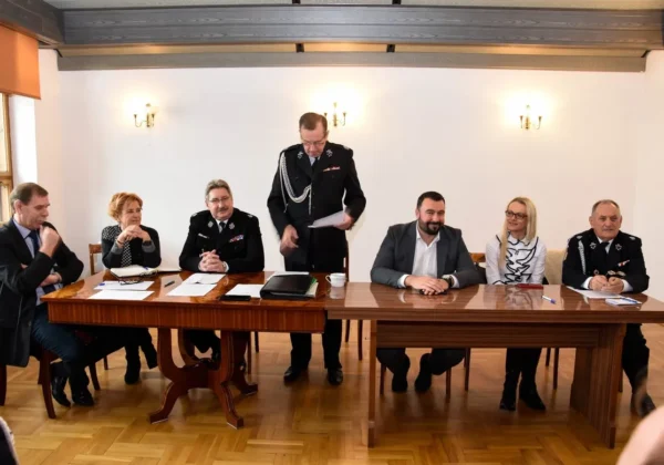 Grupa osób w mundurach strażackich i garniturach siedzi przy długim stole podczas posiedzenia Zarządu Miejsko-Gminnego ZOSP RP w Wyszogrodzie w sali konferencyjnej.