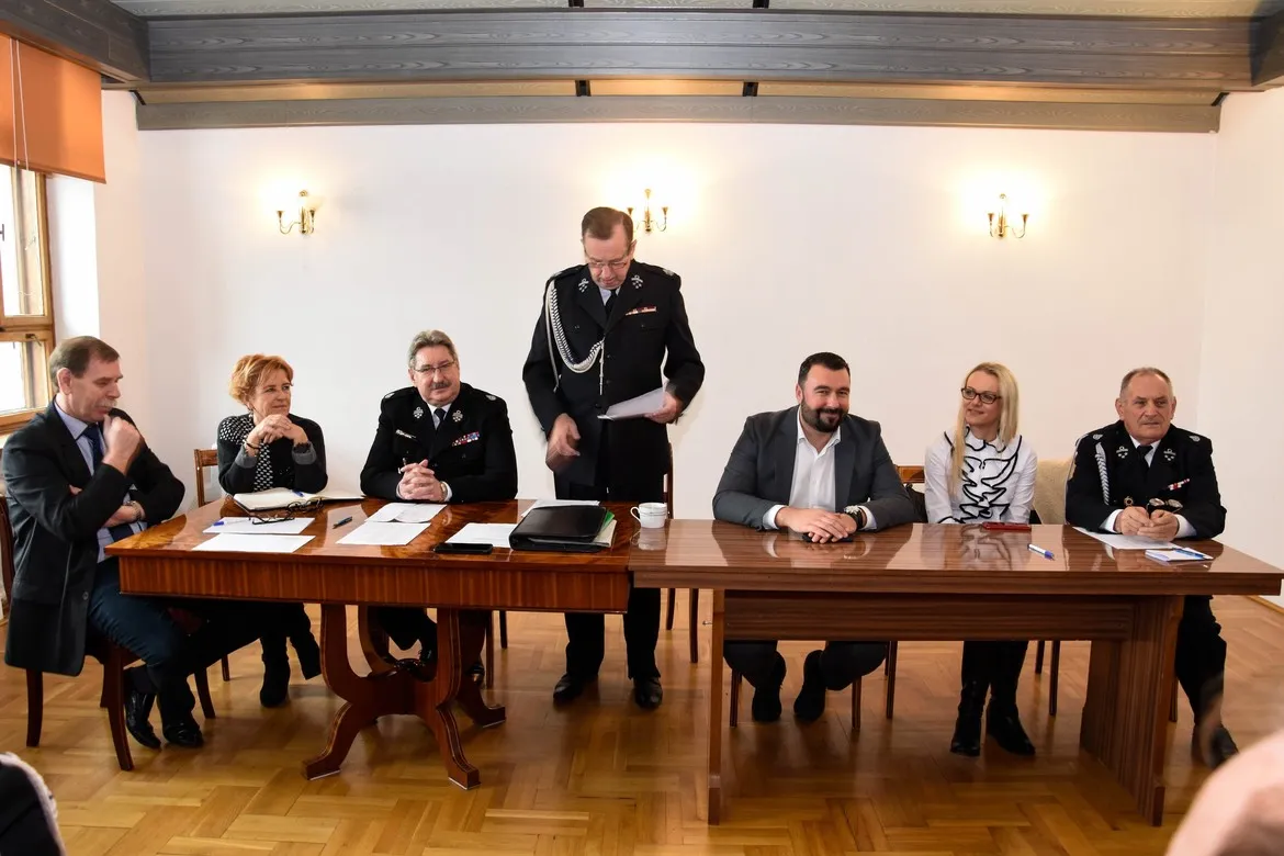 Grupa osób w mundurach strażackich i garniturach siedzi przy długim stole podczas posiedzenia Zarządu Miejsko-Gminnego ZOSP RP w Wyszogrodzie w sali konferencyjnej.