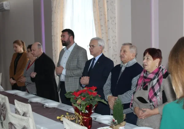 Grupa seniorów stoi przy długim stole w sali bankietowej podczas świątecznego spotkania Gminy Mała Wieś.