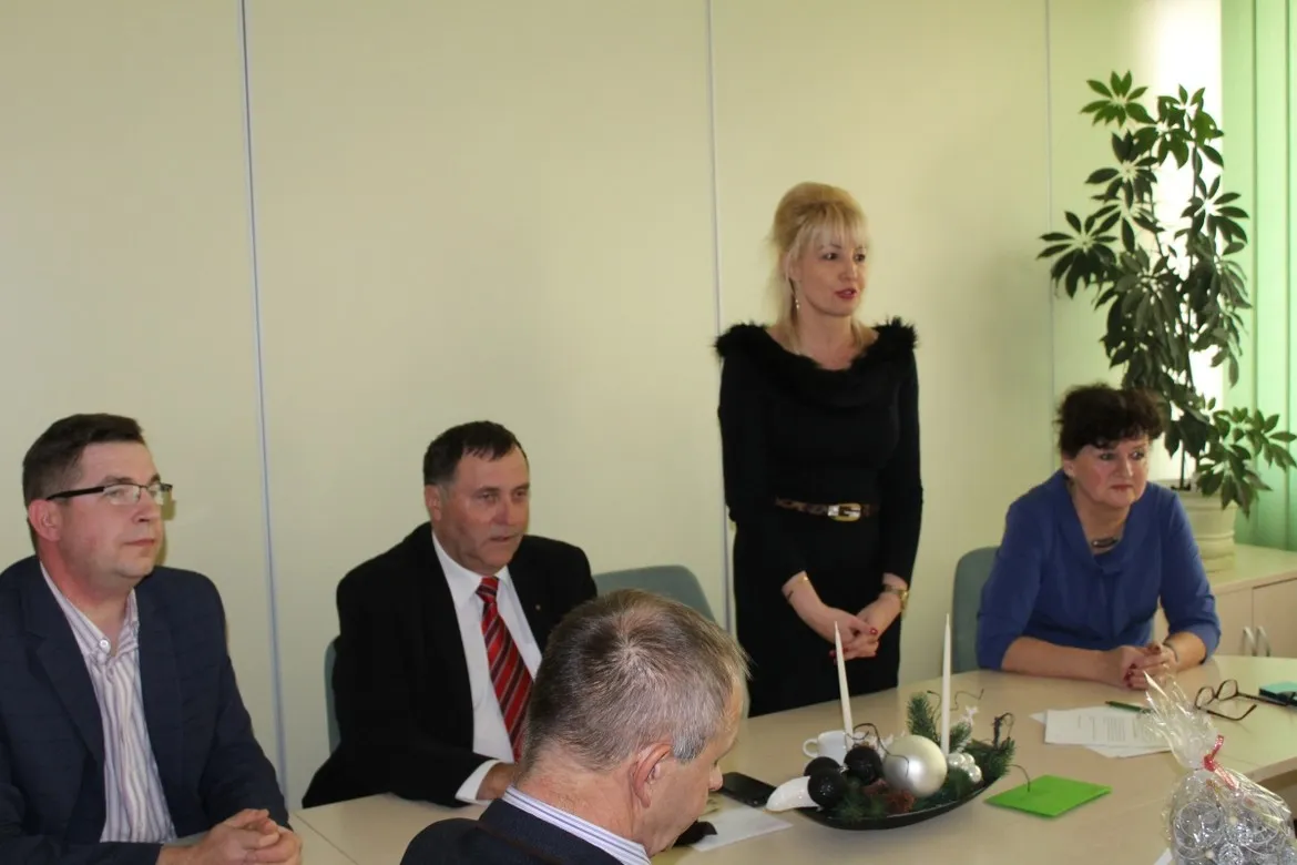 Uczestnicy spotkania wigilijnego Powiatowej Rady Rynku Pracy siedzą przy stole w jasnym biurowym pomieszczeniu, a na stole widoczne są świąteczne dekoracje.