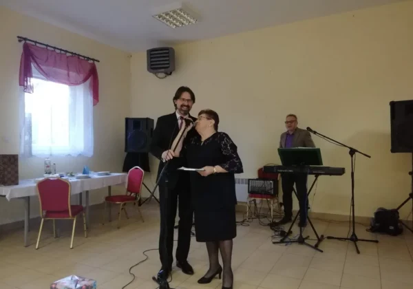 Para przy mikrofonach na scenie podczas otwarcia Klubu Senior+ w gminie Drobin, z muzykiem grającym na keyboardzie w tle.