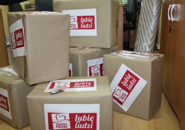 W biurze stoją zapakowane kartony opatrzone logo Szlachetna Paczka i napisem Lubię ludzi.