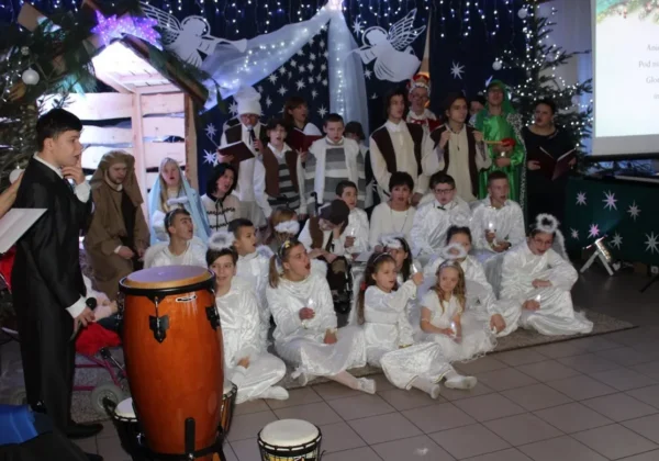 Grupa uczniów Zespołu Szkół Specjalnych w Goślicach ubranych na biało podczas opłatkowego spotkania, ustawiona w sali z bożonarodzeniowymi dekoracjami i perkusyjnymi instrumentami na pierwszym planie.