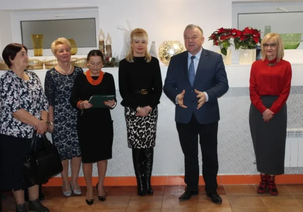 Grupa sześciu osób w eleganckich strojach stoi w holu Domu Pomocy Społecznej Nad Jarem w Nowym Miszewie podczas spotkania opłatkowego.