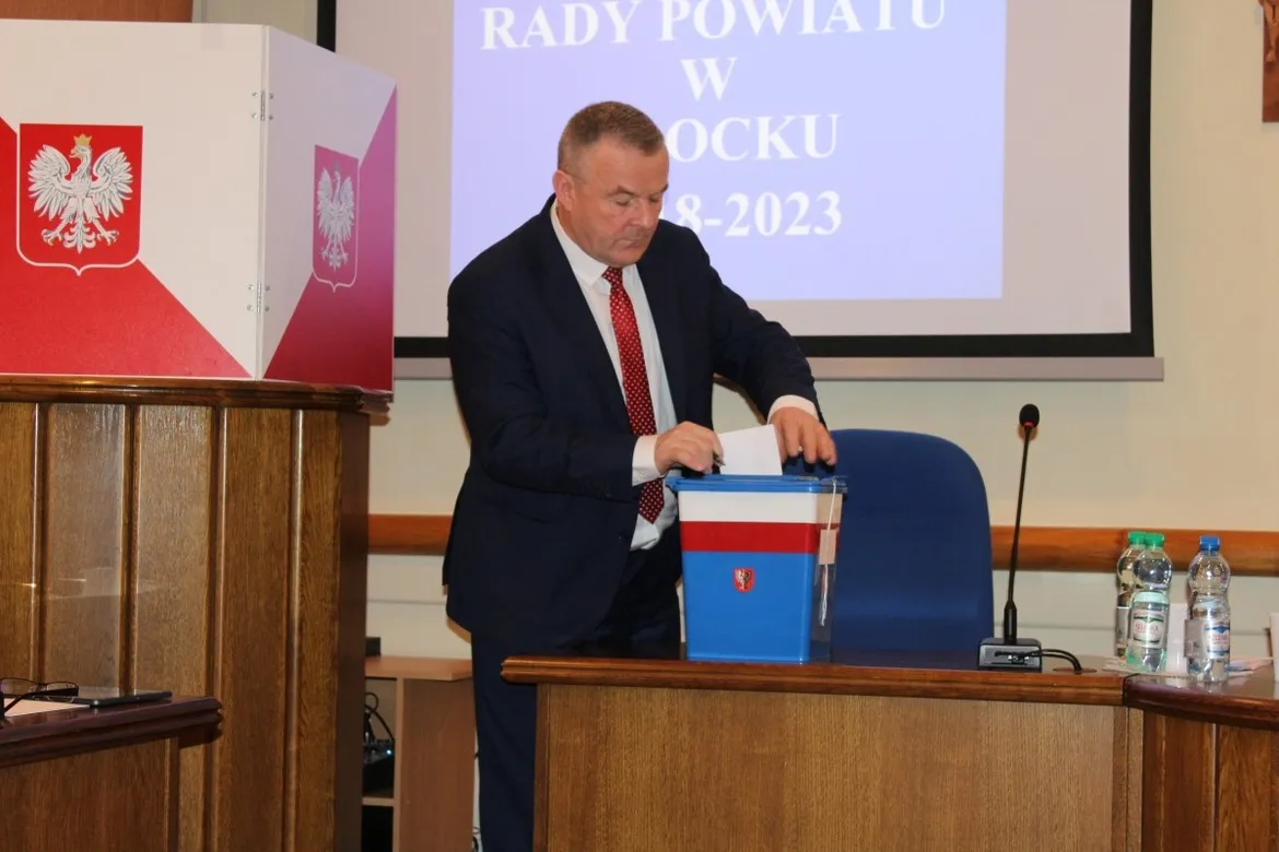 Osoba w garniturze wrzuca kartę do urny podczas II sesji Rady Powiatu w Płocku.