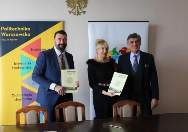 Trzy osoby w garniturach stoją przy stole, trzymają dokumenty z logo Politechniki Warszawskiej, na tle bannerów uczelni.