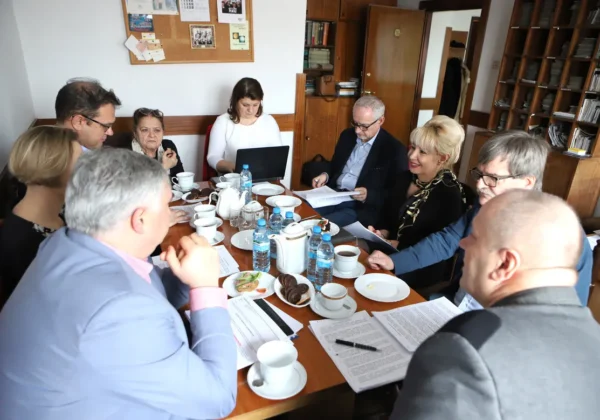 Grupa dorosłych osób siedzi przy stole w bibliotecznej sali i omawia materiały przed kolejną edycją plebiscytu „Z Tumskiego Wzgórza”.