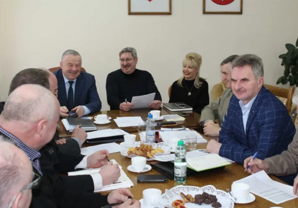 Grupa członków ZOSP RP z Płocka siedzi przy stole podczas posiedzenia Prezydium Zarządu Oddziału Powiatowego, omawiając dokumenty i notując, z kawą, wodą i przekąskami na stole.