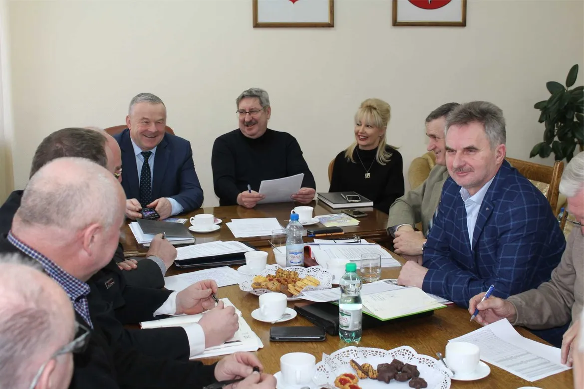 Grupa członków ZOSP RP z Płocka siedzi przy stole podczas posiedzenia Prezydium Zarządu Oddziału Powiatowego, omawiając dokumenty i notując, z kawą, wodą i przekąskami na stole.