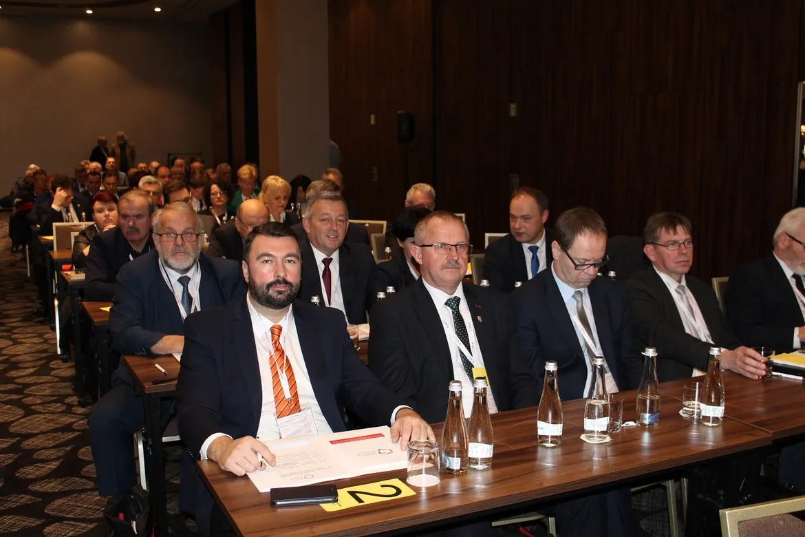 Uczestnicy XXIV Zgromadzenia Ogólnego Związku Powiatów Polskich siedzą przy stołach w sali konferencyjnej, ubrani w garnitury, z dokumentami i butelkami wody.