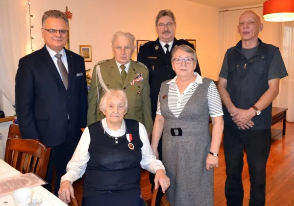 Uroczystość nadania Odznaki Jubileuszowej „Polska Niepodległa 1918–2018”: siedząca starsza kobieta z medalem otoczona pięcioma osobami stojącymi wokół.