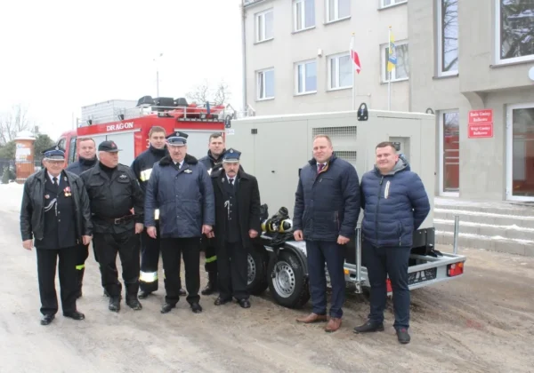 Grupa osób, w tym strażacy i urzędnicy, stoi obok przyczepy z wyposażeniem sprzętu specjalistycznego podczas przekazania go jednostkom z Gminy Bulkowo.