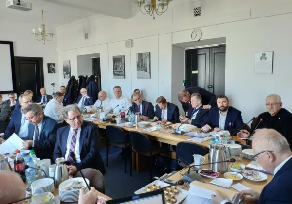 Grupa osób w garniturach siedzi przy długim stole w sali konferencyjnej podczas posiedzenia Zarządu Związku Powiatów Polskich, z mikrofonami, dokumentami i poczęstunkiem na stole.