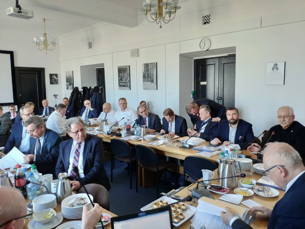 Grupa osób w garniturach siedzi przy długim stole w sali konferencyjnej podczas posiedzenia Zarządu Związku Powiatów Polskich, z mikrofonami, dokumentami i poczęstunkiem na stole.