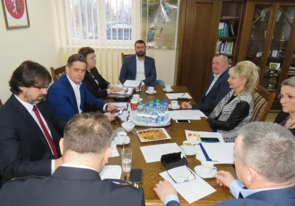 Grupa osób w garniturach siedzi przy stole w sali konferencyjnej, omawiając kwestie bezpieczeństwa pożarowego w 2018 roku.