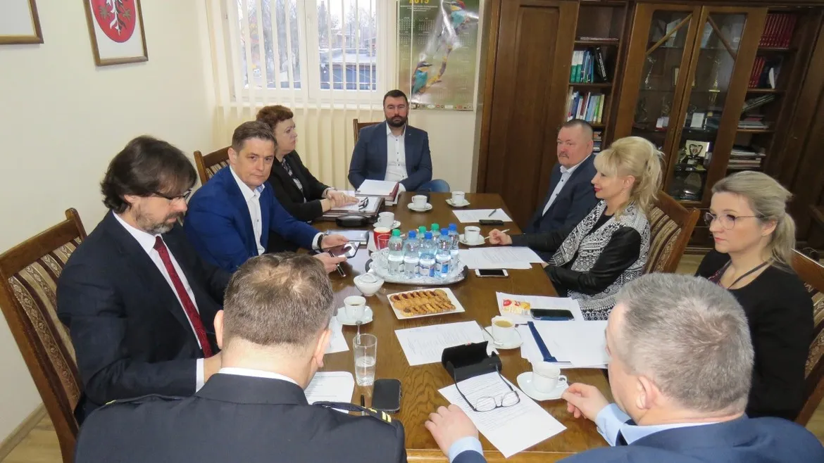 Grupa osób w garniturach siedzi przy stole w sali konferencyjnej, omawiając kwestie bezpieczeństwa pożarowego w 2018 roku.