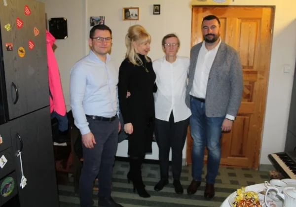 Cztery dorosłe osoby stoją razem w domowym wnętrzu, przy stole z przekąskami i herbatą, świętując 60 lat.