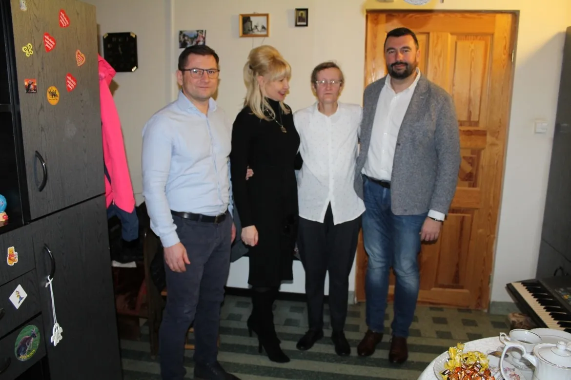 Cztery dorosłe osoby stoją razem w domowym wnętrzu, przy stole z przekąskami i herbatą, świętując 60 lat.