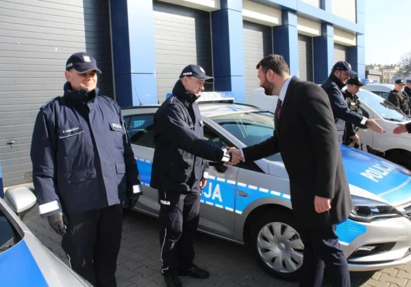 Nowy radiowóz policji w powiecie płockim w Wyszogrodzie podczas prezentacji; policjanci w mundurach witają gościa i dochodzi do uścisku dłoni.
