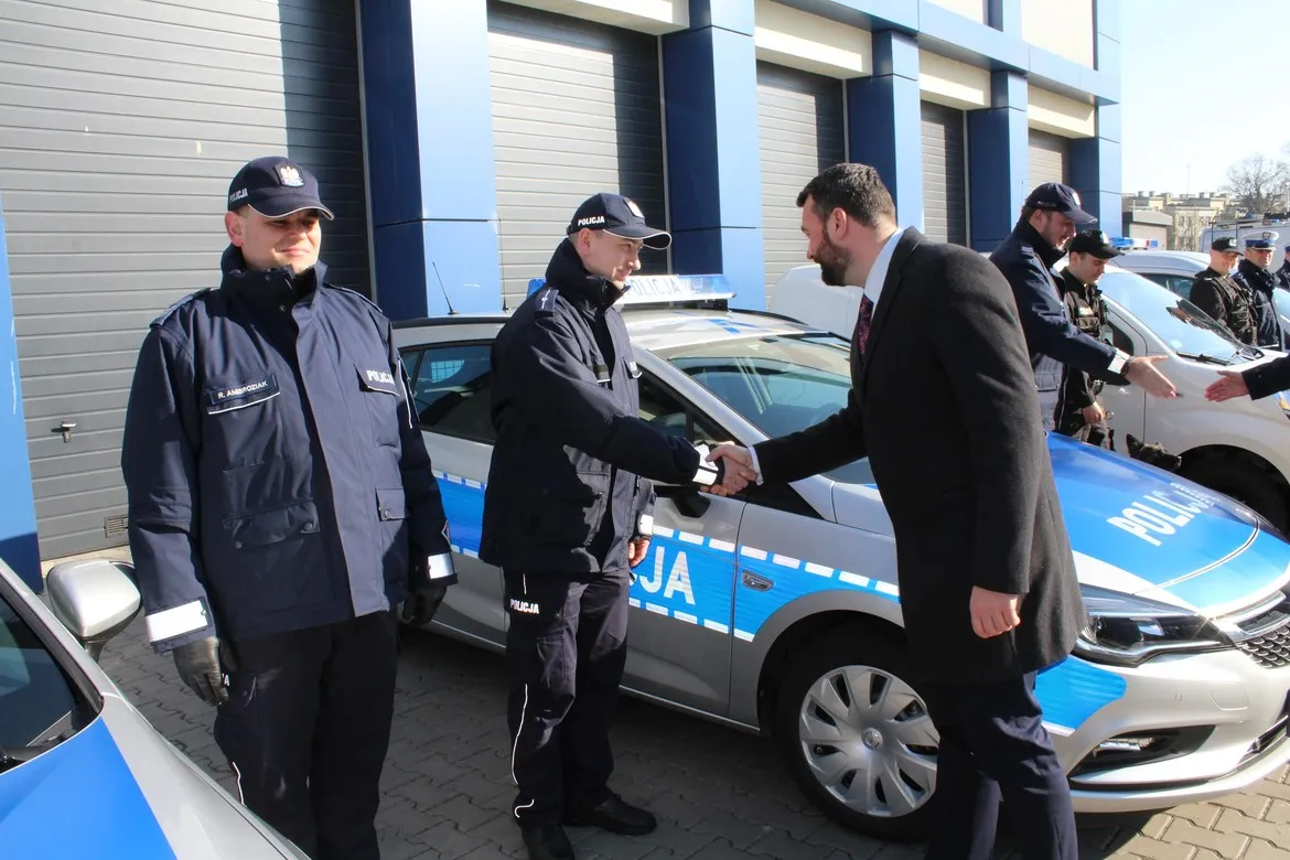 Nowy radiowóz policji w powiecie płockim w Wyszogrodzie podczas prezentacji; policjanci w mundurach witają gościa i dochodzi do uścisku dłoni.