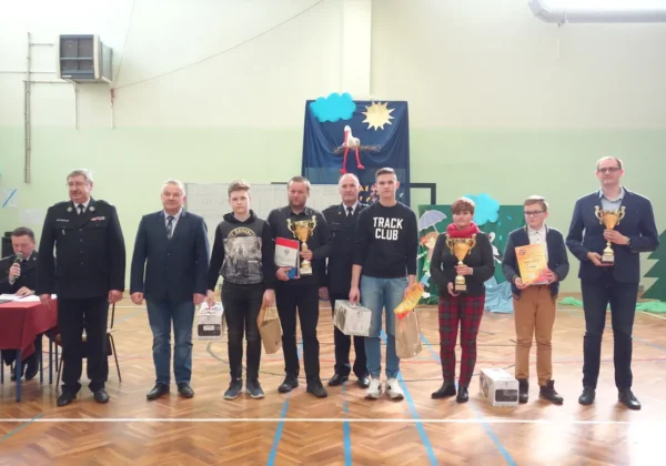 Grupa uczestników i laureatów eliminacji powiatowych XLII edycji Ogólnopolskiego Turnieju Wiedzy Pożarniczej stoi na sali gimnastycznej, prezentując trofea, dyplomy i nagrody.