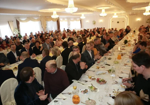 Duża hala bankietowa wypełniona gośćmi siedzącymi przy długich stołach zastawionych jedzeniem i napojami podczas spotkania Sołtysów Powiatu Płockiego – liderów rozwoju lokalnego.