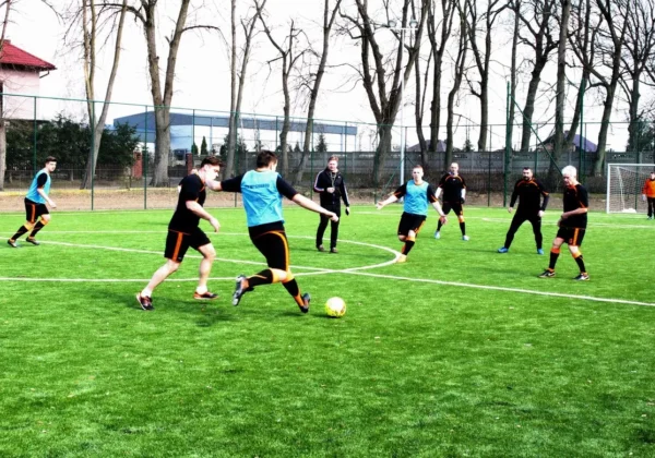 Grupa mężczyzn gra w piłkę nożną na nowym boisku z sztucznej trawy w Wyszogrodzie podczas jego otwarcia.