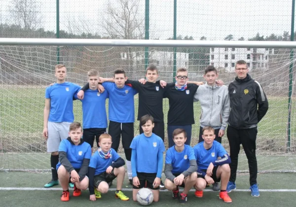 Grupa młodych piłkarzy w niebieskich koszulkach wraz z trenerem stoi i klęka przed bramką na boisku podczas Turnieju Piłki Nożnej o Puchar Starosty Płockiego.