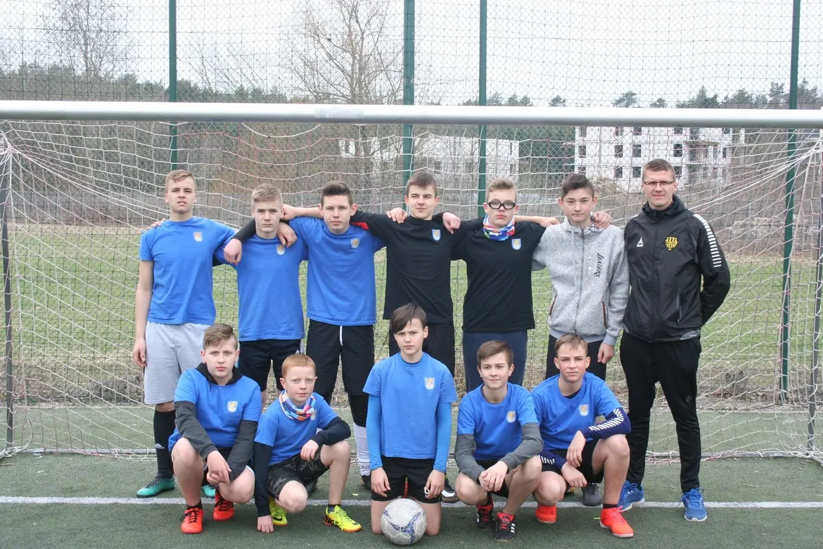 Grupa młodych piłkarzy w niebieskich koszulkach wraz z trenerem stoi i klęka przed bramką na boisku podczas Turnieju Piłki Nożnej o Puchar Starosty Płockiego.