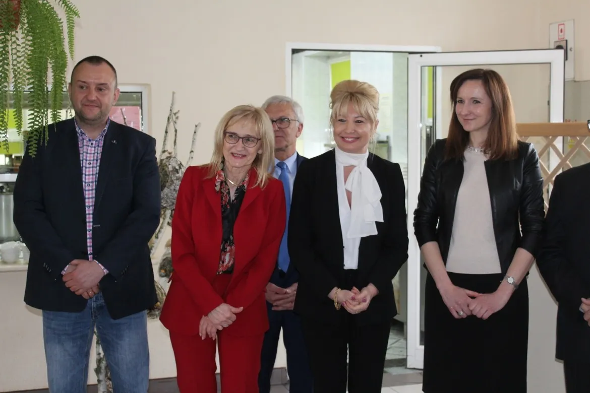 Pięć uśmiechniętych osób w eleganckich strojach stoi w holu podczas świątecznego spotkania w Zakrzewie.