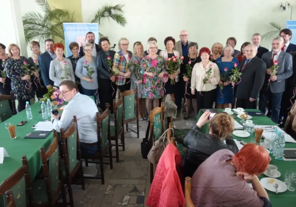 Grupa członków ZNP z Płocka stoi w sali konferencyjnej podczas Konferencji Sprawozdawczo-Wyborczej Oddziału Powiatowego ZNP w Płocku, trzymając róże i pozując do zdjęcia.