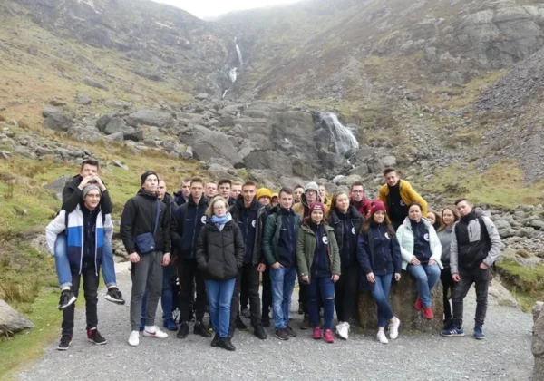 Grupa uczniów Zespołu Szkół im. Jana Śniadeckiego w Wyszogrodzie stoi na skalistej drodze w górach z wodospadem w tle podczas wyjazdu na praktyki zawodowe.
