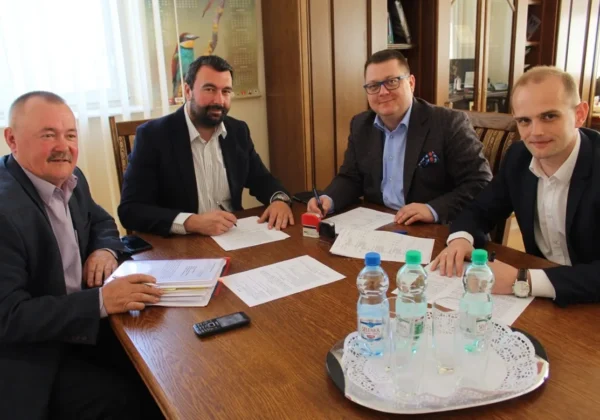 Czterech mężczyzn w garniturach siedzi przy stole i podpisuje dokumenty podczas spotkania dotyczącego wspólnej inwestycji Powiatu Płockiego i Gminy Radzanowo.
