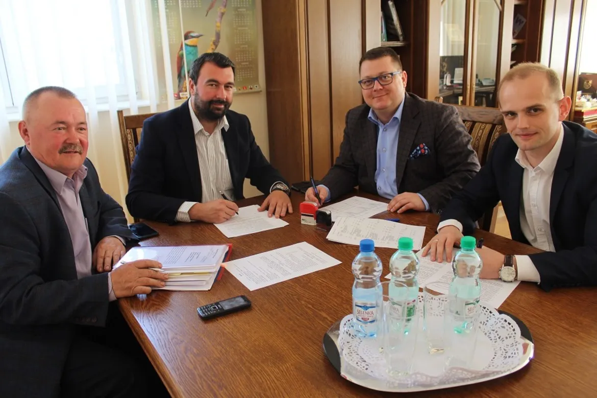 Czterech mężczyzn w garniturach siedzi przy stole i podpisuje dokumenty podczas spotkania dotyczącego wspólnej inwestycji Powiatu Płockiego i Gminy Radzanowo.