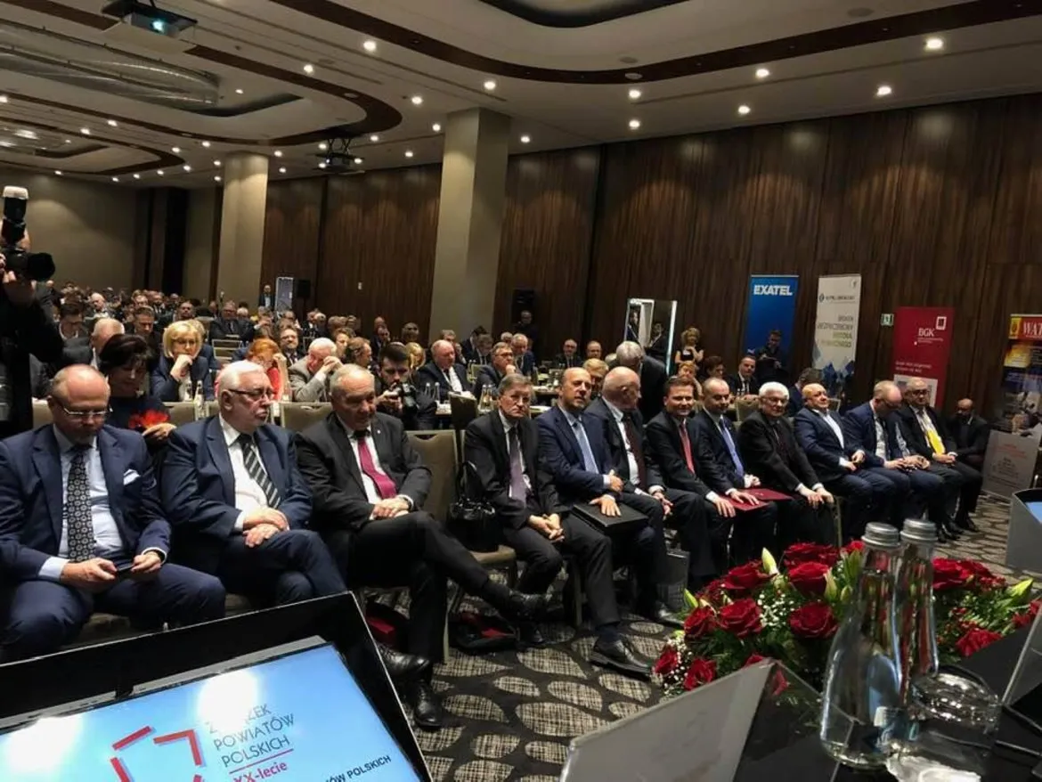Uczestnicy w garniturach siedzą w pierwszym rzędzie podczas XXV Zgromadzenia Ogólnego Związku Powiatów Polskich w sali konferencyjnej.