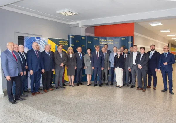 Grupa osób w garniturach stoi razem w korytarzu przed banerami Politechniki Warszawskiej podczas spotkania Rady ds. Partnerstwa Gospodarczo-Społecznego na PW.